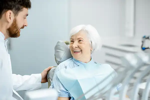 Dentist speaking to smiling dental patient sitting in exam chair Dentist speaking to smiling dental patient sitting in exam chair