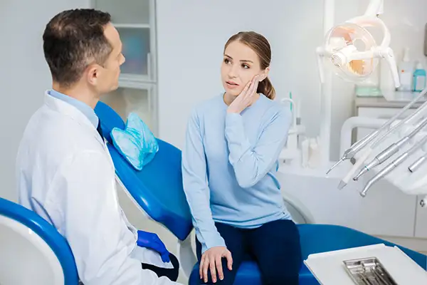 Concerned white patient discussing her tooth pain with her dentist while sitting in a dental chair Concerned white patient discussing her tooth pain with her dentist while sitting in a dental chair
