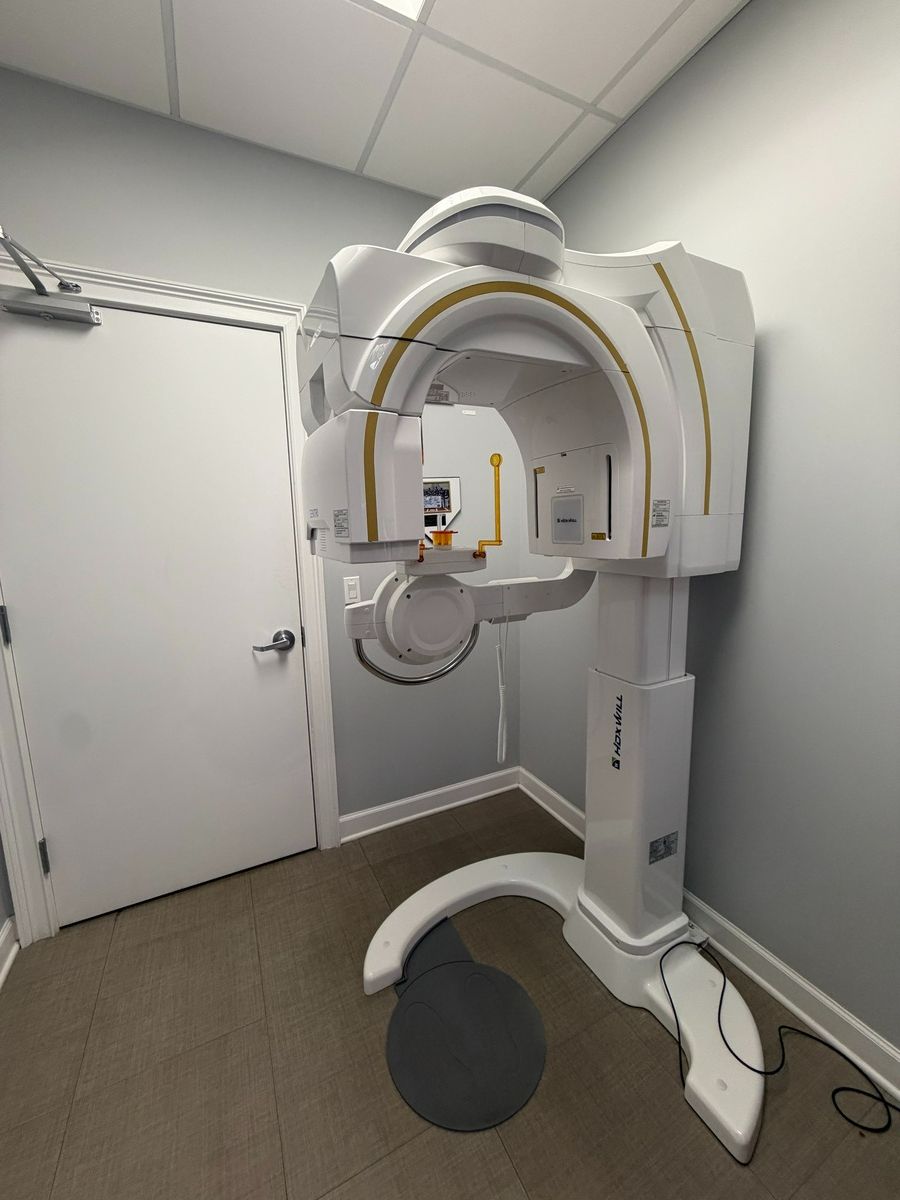 Dentist wearing a labcoat and gloves reaches out to touch a futuristic hologram of a tooth Dental imaging room with an HDX WILL X-ray machine.