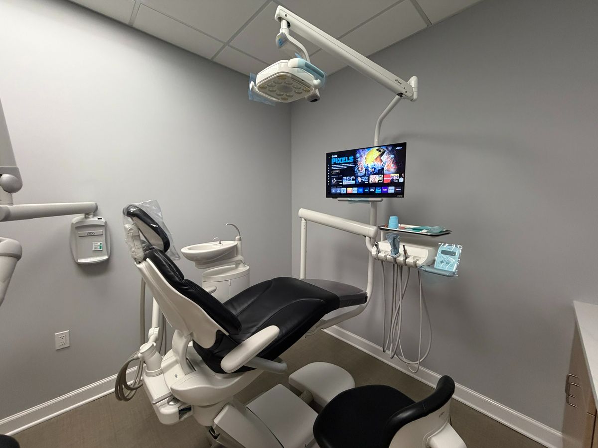 Dental chair with an overhead light, instrument unit, and patient-facing screen.