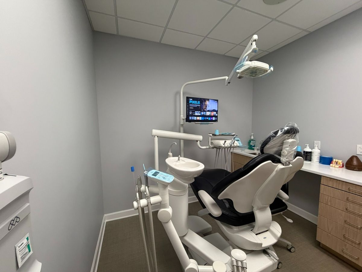 Dental treatment room with a dental chair, instruments, countertop, and storage cabinets.